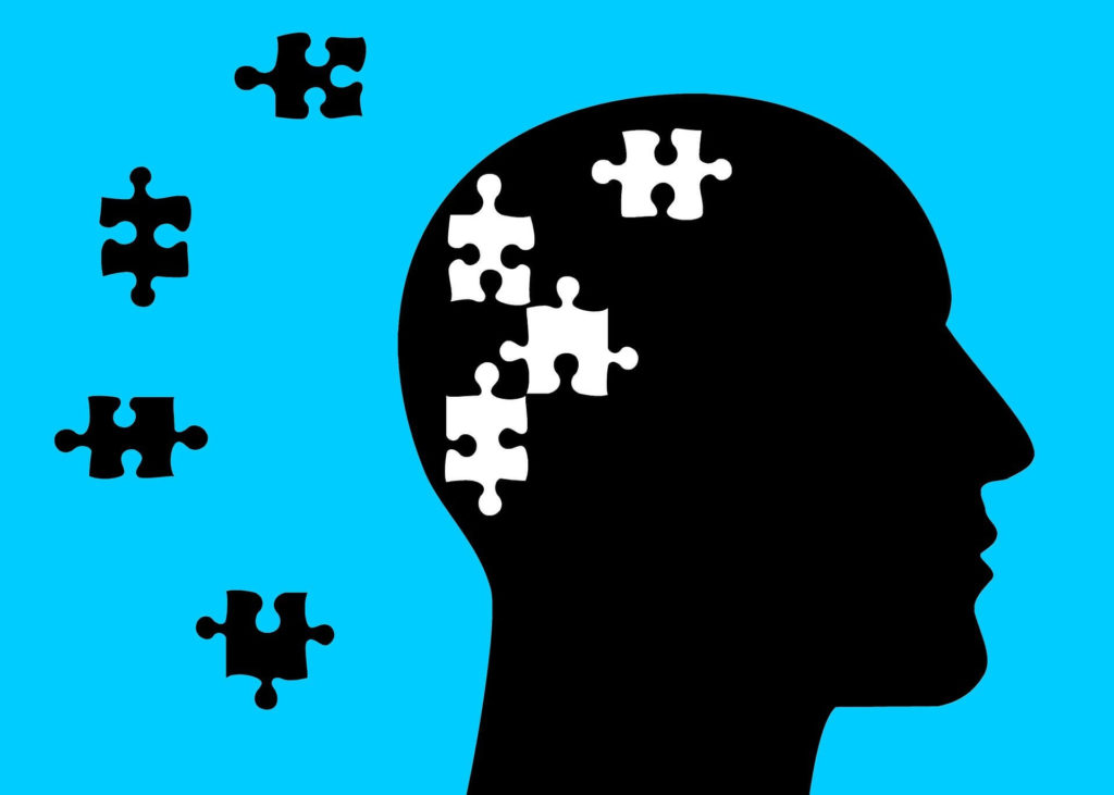 Profil de tête humaine dans laquelle 4 pièces de puzzle sont dessinées. Sur le fond, à côté de la tête, ces 4 mêmes pièces sont aussi dessinées comme si elles avaient été découpées depuis le cerveau et dispersées sur l’arrière-plan.
