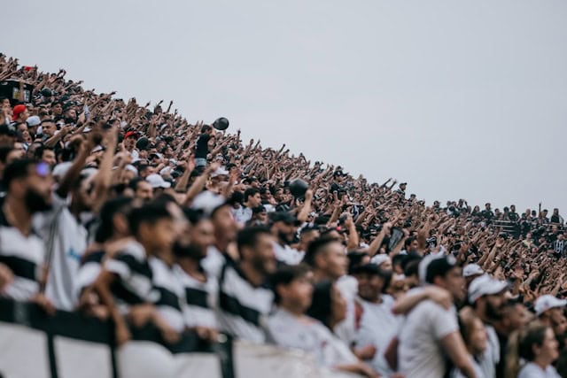 Une foule de personnes dans des gradins, dont une majorité lève les bras.